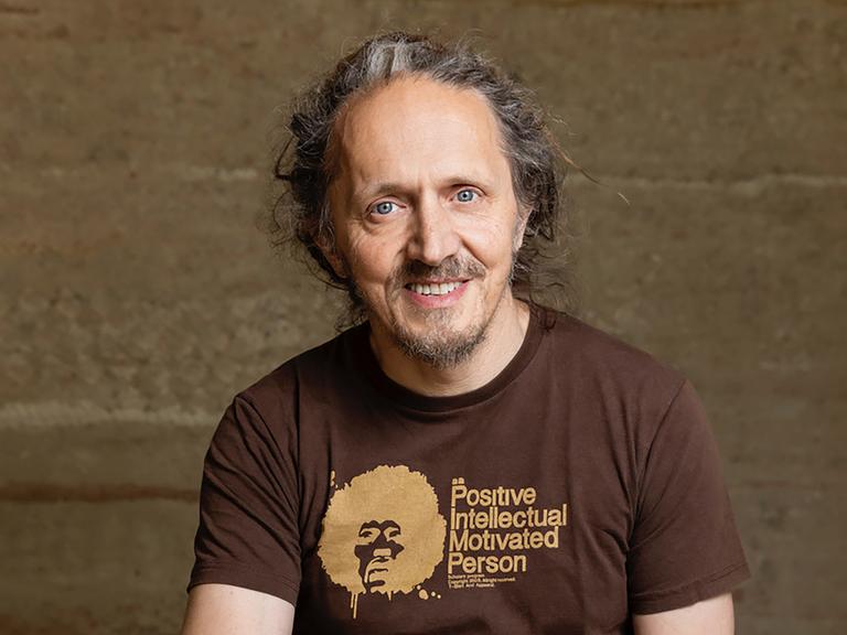 Harry Putz trägt ein braunes´T-Shirt mit der Aufschrift "Positive Intellectual Person" und schaut freundlich in die Kamera.