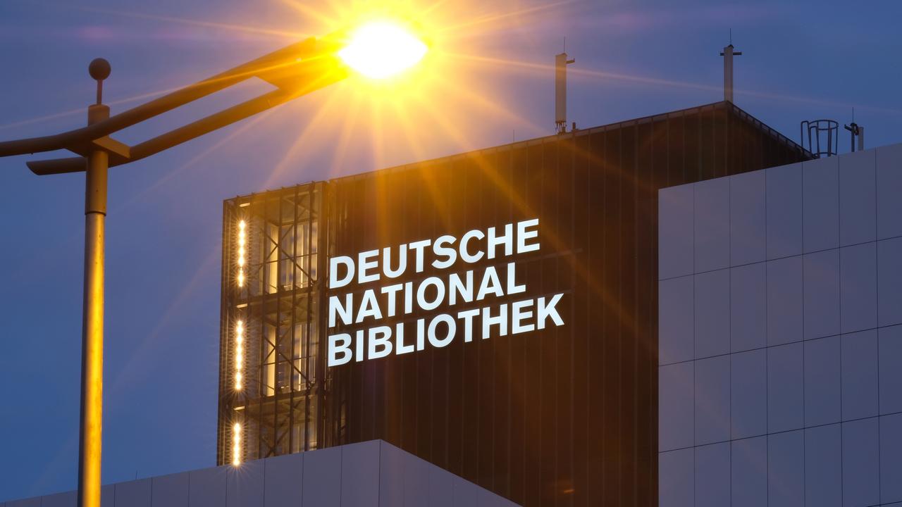 Der neue Schriftzug "Deutsche Nationalbibliothek" leuchtet in Leipzig an einem 55 Meter hohen Gebäude der früheren Deutschen Bücherei mit einer Straßenlaterne im Vordergrund. 