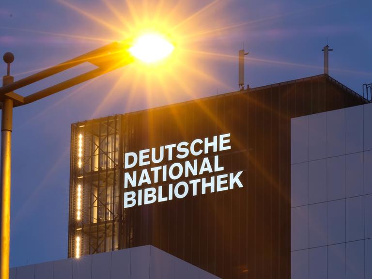 Der neue Schriftzug "Deutsche Nationalbibliothek" leuchtet in Leipzig an einem 55 Meter hohen Gebäude der früheren Deutschen Bücherei mit einer Straßenlaterne im Vordergrund. 