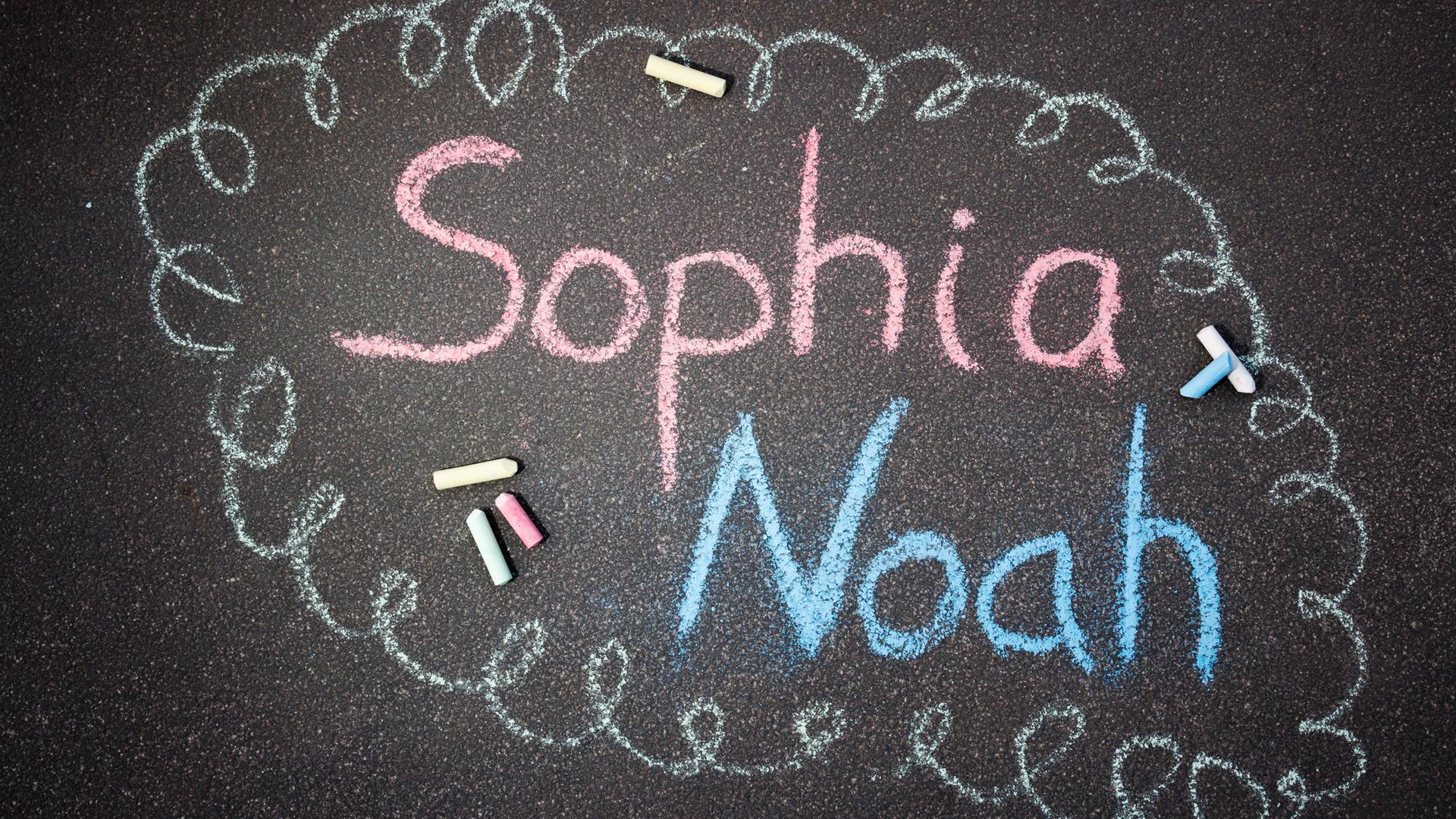 Mit Straßenkreide sind die Namen Sophia und Noah auf den Boden geschrieben. Mit Straßenkreide sind die Namen Sophia und Noah auf den Boden geschrieben.