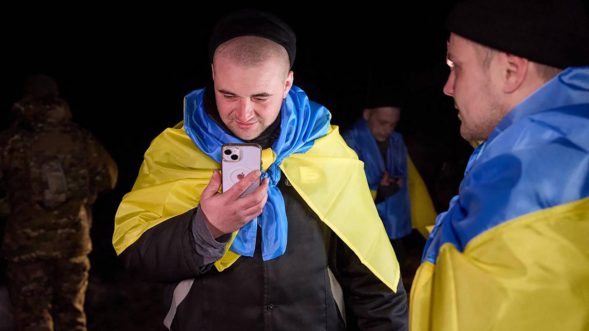 Ein Mann in Soldatenuniform, der in eine blau-gelbe ukrainische Flagge gehüllt ist, hält ein Smartphone in der Hand.