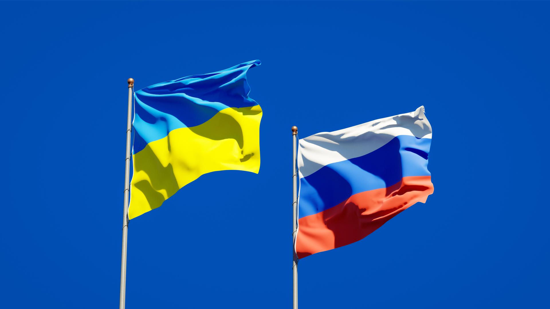 Die Flaggen von Russland und der Ukrainie wehen vor einem blauen Himmel.