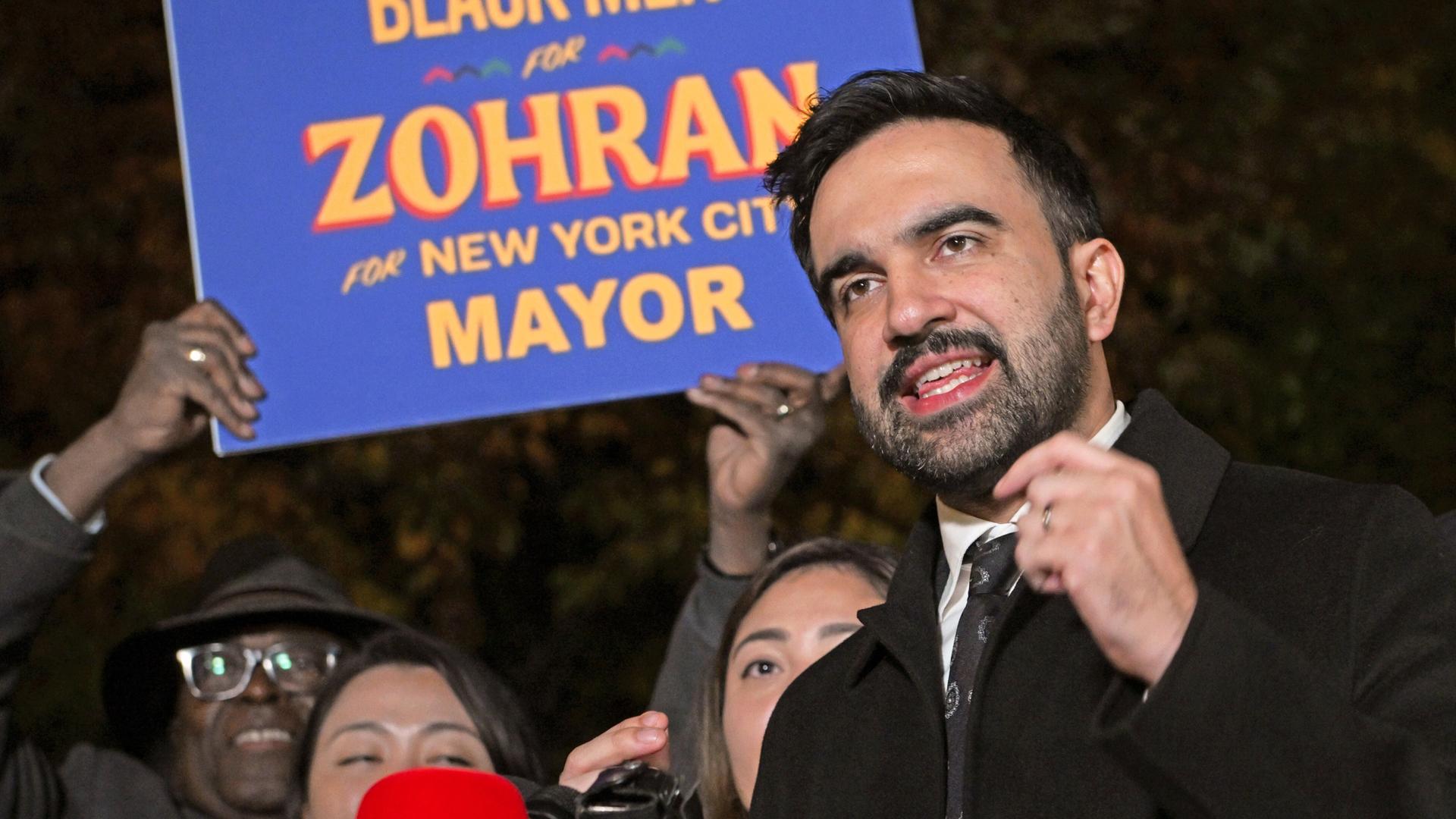 Zohran Mamdani spricht am 3. November 2025 in Astoria, Queens vor Anhängern in Mikrofone. Hinter ihm wird ein Schild mit der Aufschrift "Zohran for New York City Mayor" Zohran Mamdani spricht am 3. November 2025 in Astoria, Queens vor Anhängern in Mikrofone. Hinter ihm wird ein Schild mit der Aufschrift "Zohran for New York City Mayor"