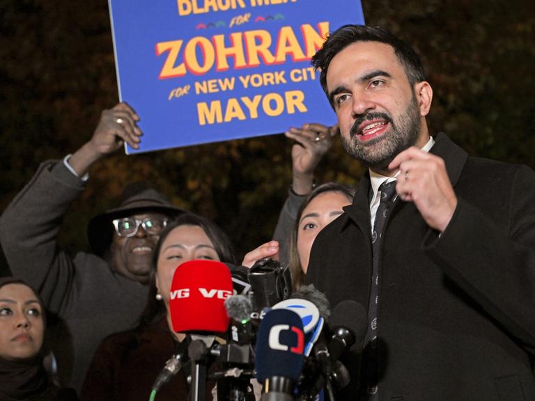 Zohran Mamdani spricht am 3. November 2025 in Astoria, Queens vor Anhängern in Mikrofone. Hinter ihm wird ein Schild mit der Aufschrift "Zohran for New York City Mayor" Zohran Mamdani spricht am 3. November 2025 in Astoria, Queens vor Anhängern in Mikrofone. Hinter ihm wird ein Schild mit der Aufschrift "Zohran for New York City Mayor"