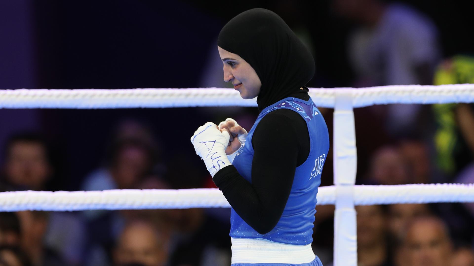 Eine Boxerin mit schwarzem Hijab steht im Boxring und ballt die Fäuste. Eine Boxerin mit schwarzem Hijab steht im Boxring und ballt die Fäuste.
