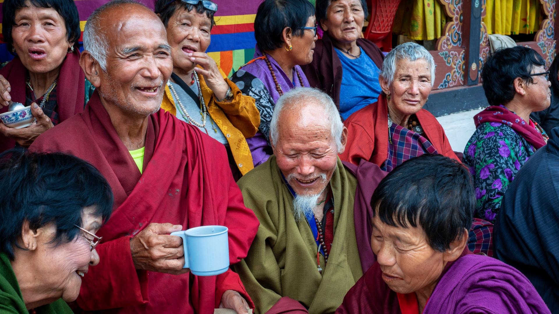 Gläubige Buddhisten in traditioneller Kleidung. Wollene Mäntel in Dunkelrot und Olivgrün. Die älteren Menschen unterhalten sich, viele lächeln. Ein Mann hält eine Tasse in der Hand. Alle machen einen zufriedenen Eindruck
Gläubige Buddhisten in traditioneller Kleidung. Wollene Mäntel in Dunkelrot und Olivgrün. Die älteren Menschen unterhalten sich, viele lächeln. Ein Mann hält eine Tasse in der Hand. Alle machen einen zufriedenen Eindruck