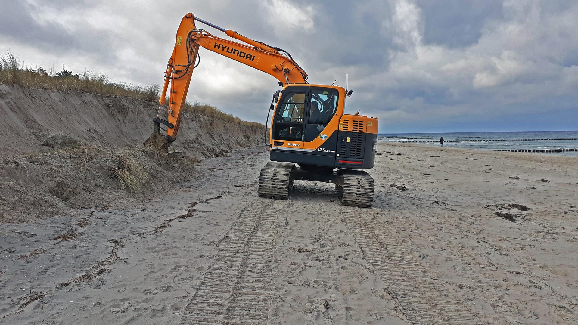 Nach der schweren Sturmflut vom 20. und 21.Oktober 2023 werden die Schaeden sichtbar - ein Bagger glättet die beschädigten Dünen am Ostseestrand in Zingst.