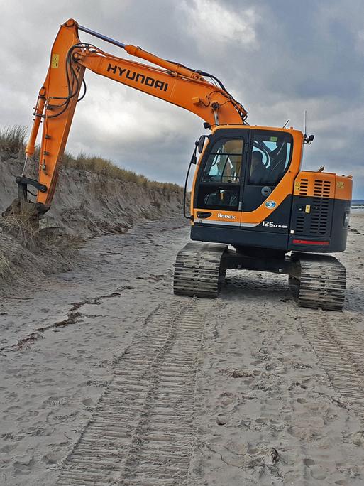 Nach der schweren Sturmflut vom 20. und 21.Oktober 2023 werden die Schaeden sichtbar - ein Bagger glättet die beschädigten Dünen am Ostseestrand in Zingst.