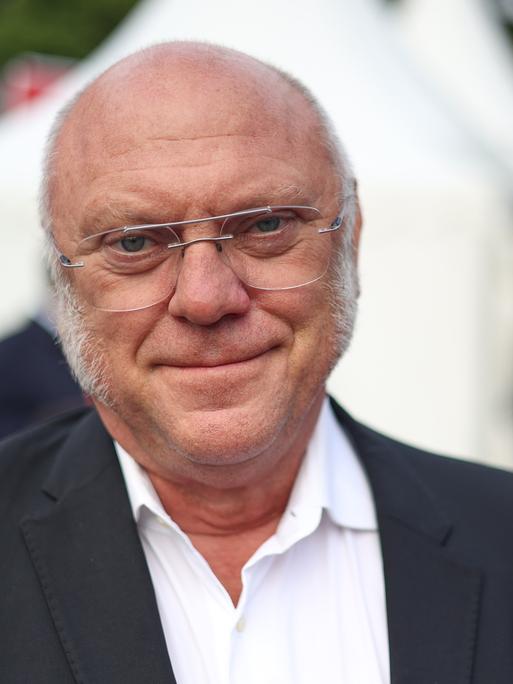 Ulrich Schneider mit weißen Haaren und Metallbrille trägt einen Anzug und schaut freundlich in die Kamera