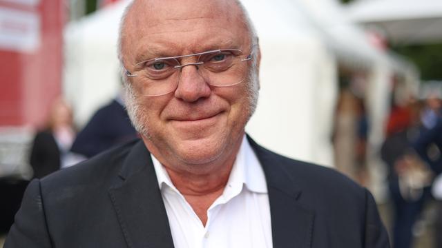 Ulrich Schneider mit weißen Haaren und Metallbrille trägt einen Anzug und schaut freundlich in die Kamera