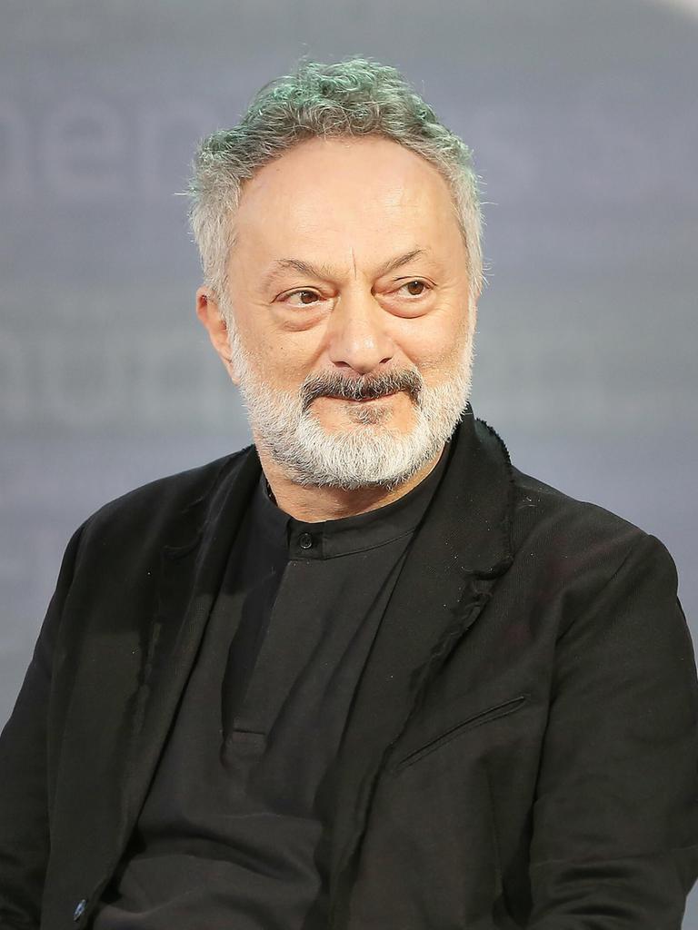 Feridun Zaimoglu sitzt vor einem grauen Hintergrund und guckt an der Kamera vorbei