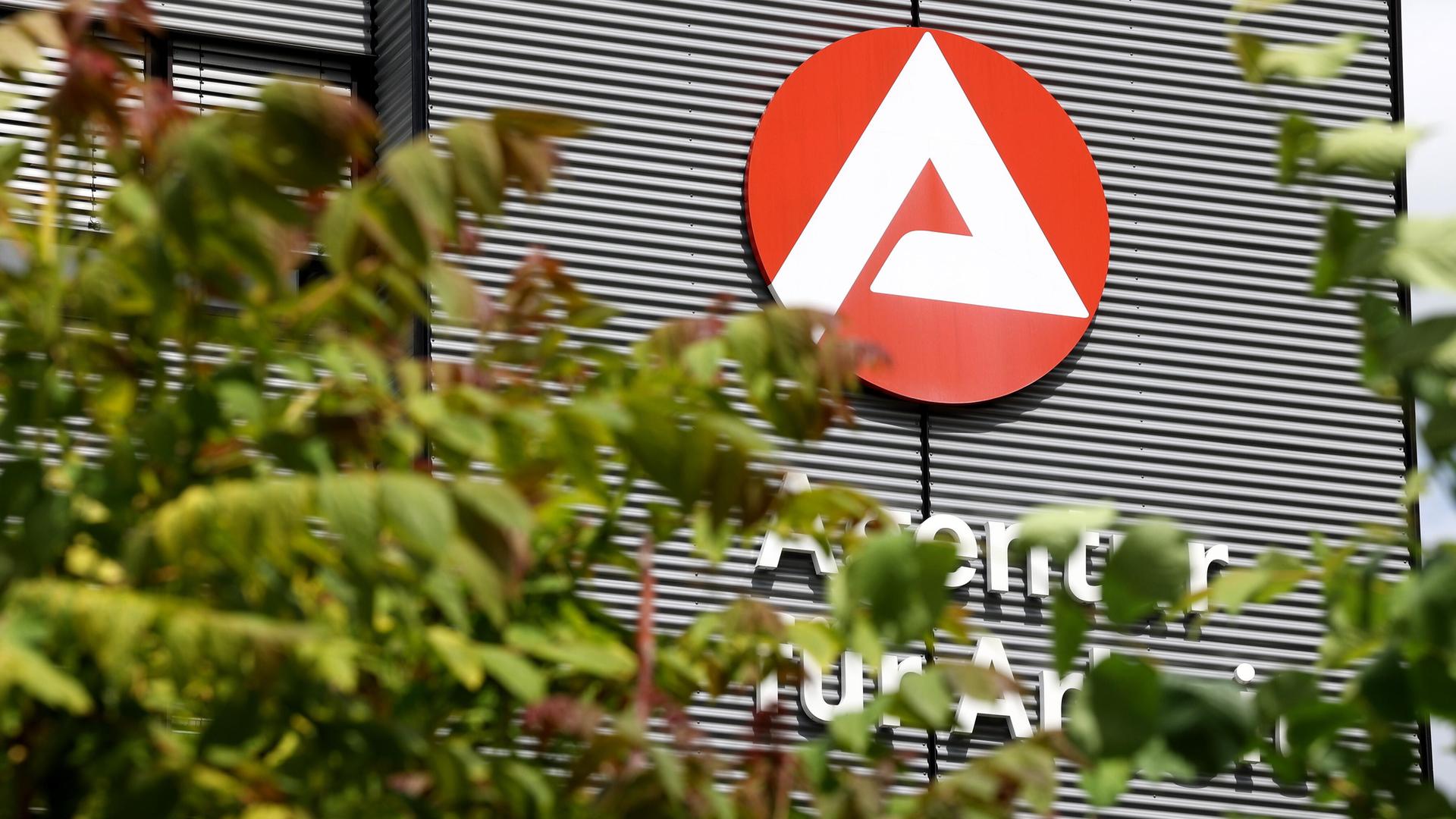 Gebäude mit Logo und Schriftzug der Agentur für Arbeit, teilweise verdeckt von Bäumen Gebäude mit Logo und Schriftzug der Agentur für Arbeit, teilweise verdeckt von Bäumen
