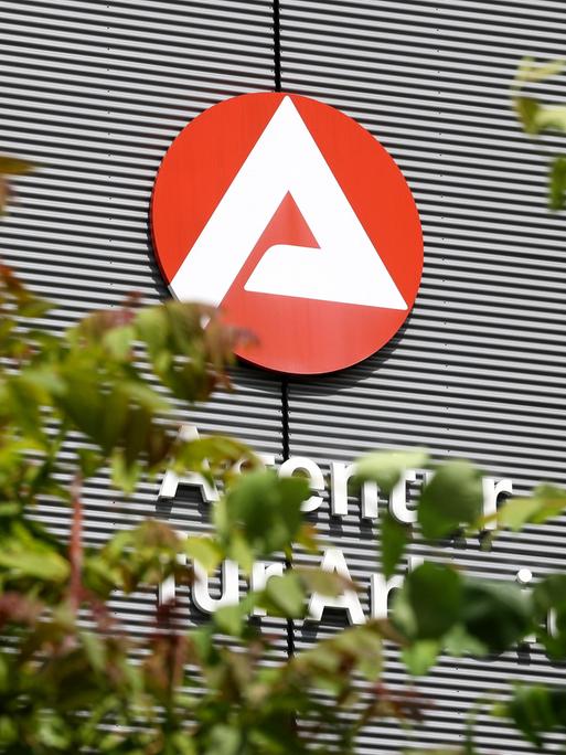 Gebäude mit Logo und Schriftzug der Agentur für Arbeit, teilweise verdeckt von Bäumen 
