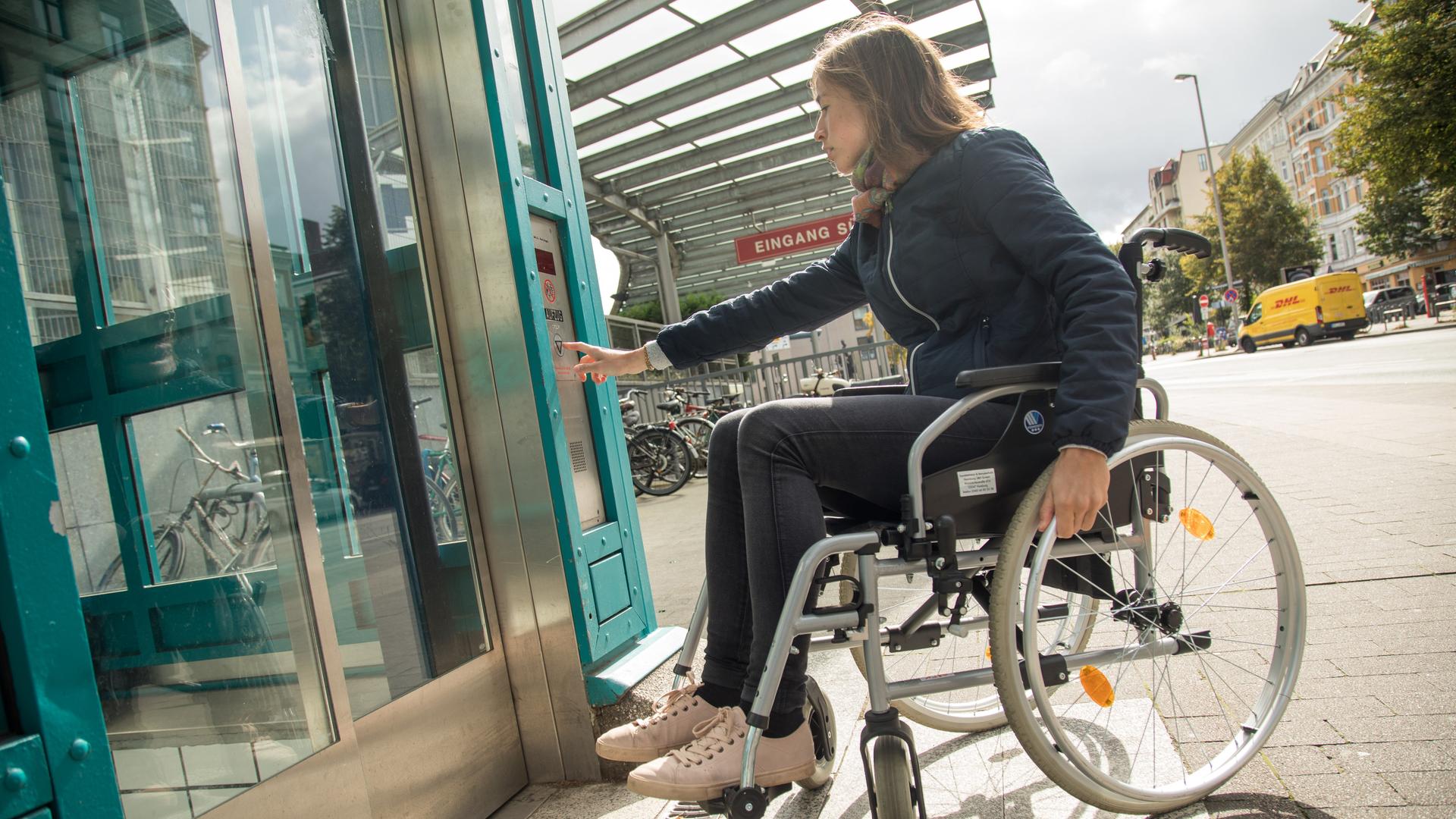 Eine Frau im Rollstuhl öffnet einen Fahrstuhl.