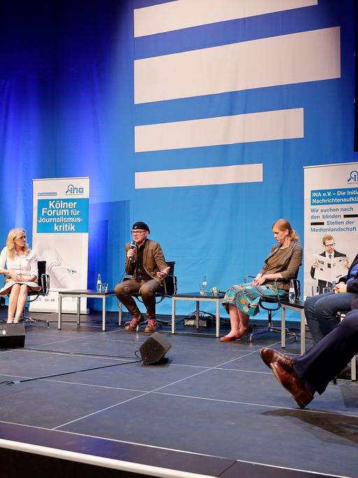Die Gäste und der Moderator des Panels sitzen auf der Bühne vor einem großen Deutschlandfunk-Logo.