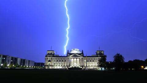 Ein Blitz erscheint am Himmel über dem beleuchteten Reichstagsgebäude in Berlin