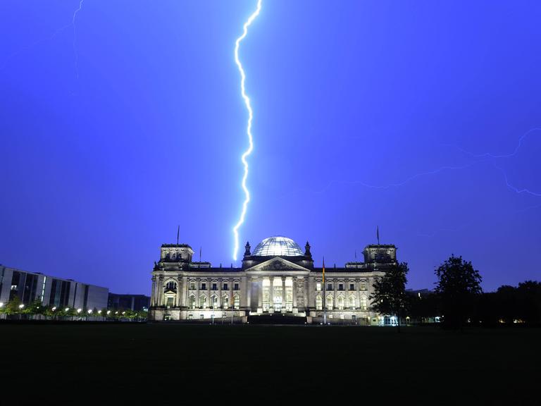 Ein Blitz erscheint am Himmel über dem beleuchteten Reichstagsgebäude in Berlin