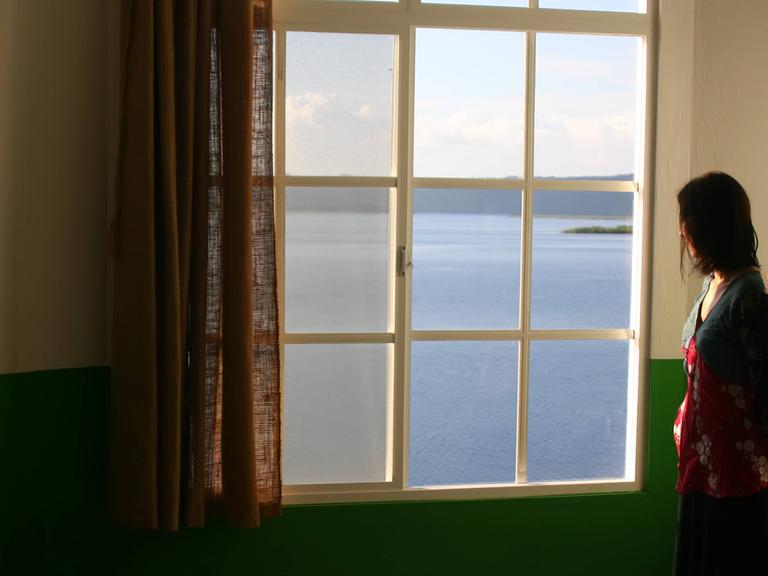 Eine Frau steht allein am Fenster.