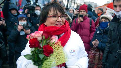 Yulia Galyamina steht lächelnd mit einem Blumenstrauß in Händen vor Pressevertretern auf der Straße.