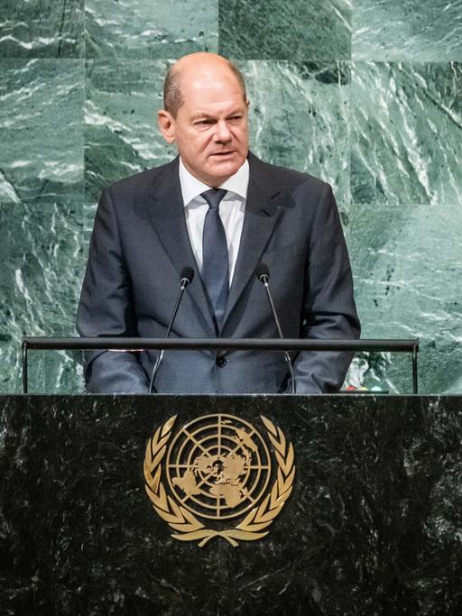 Bundeskanzler Olaf Scholz steht an einem Rednerpult, auf der Trennwand zum Publikum ist das goldene Wappen der Vereinten Nationen zu sehen.