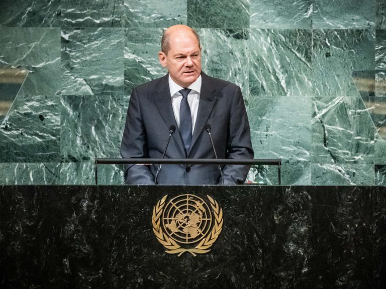 Bundeskanzler Olaf Scholz steht an einem Rednerpult, auf der Trennwand zum Publikum ist das goldene Wappen der Vereinten Nationen zu sehen.