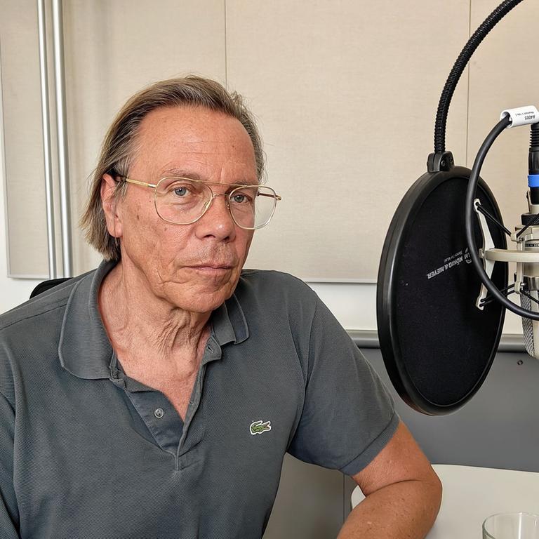 Harald Welzer, ein älterer Mann mit Brille, sitzt vor einem Studiomikrofon und guckt in die Kamera.