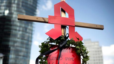 Eine Frau hält ein Kreuz in der Hand, auf dem das Apotheken-Logo angebracht ist.