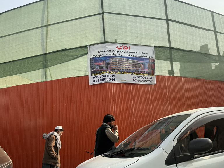 Ein Schild an einem orangenen Bauzaun an einer Straße in Kabul