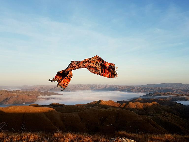 Ein buntes Tuch fliegt in der Luft über einen See. 