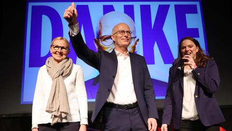 Peter Tschentscher steht mit Parteifreundinnen auf einer Bühne vor SPD-Anhängern. Mit seiner rechten Hand zeigt er ein "Daumen-hoch-Symbol". Im Hintergrund ist eine Projektion seines Gesichtes mit einen großen "Danke"-Schriftzug zu sehen. 