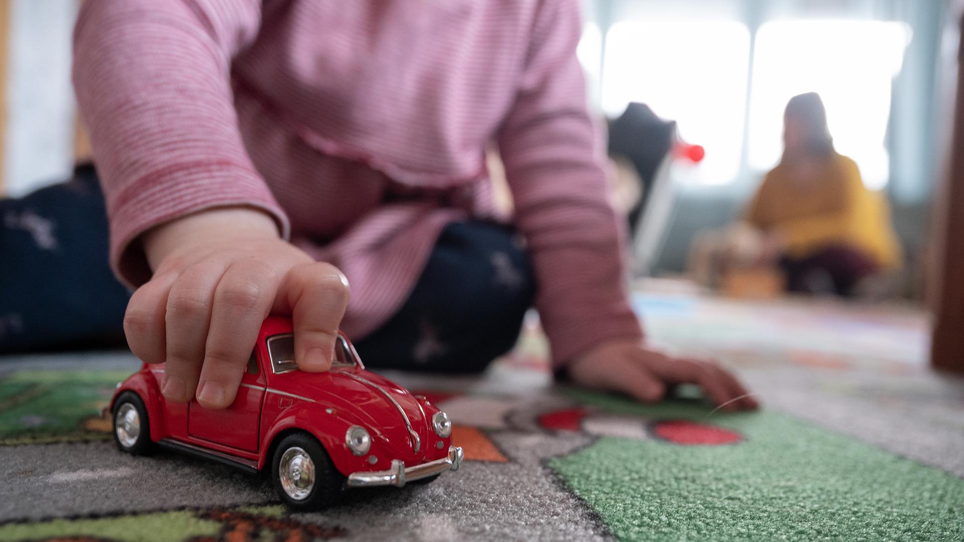 Ein Kind spielt zu Hause mit einem roten Spielzeugauto. 