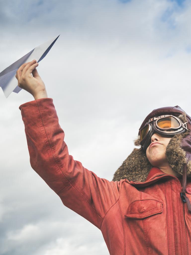 Ein Junge in Pilotenkostüm hält einen Papierflieger in die Luft.