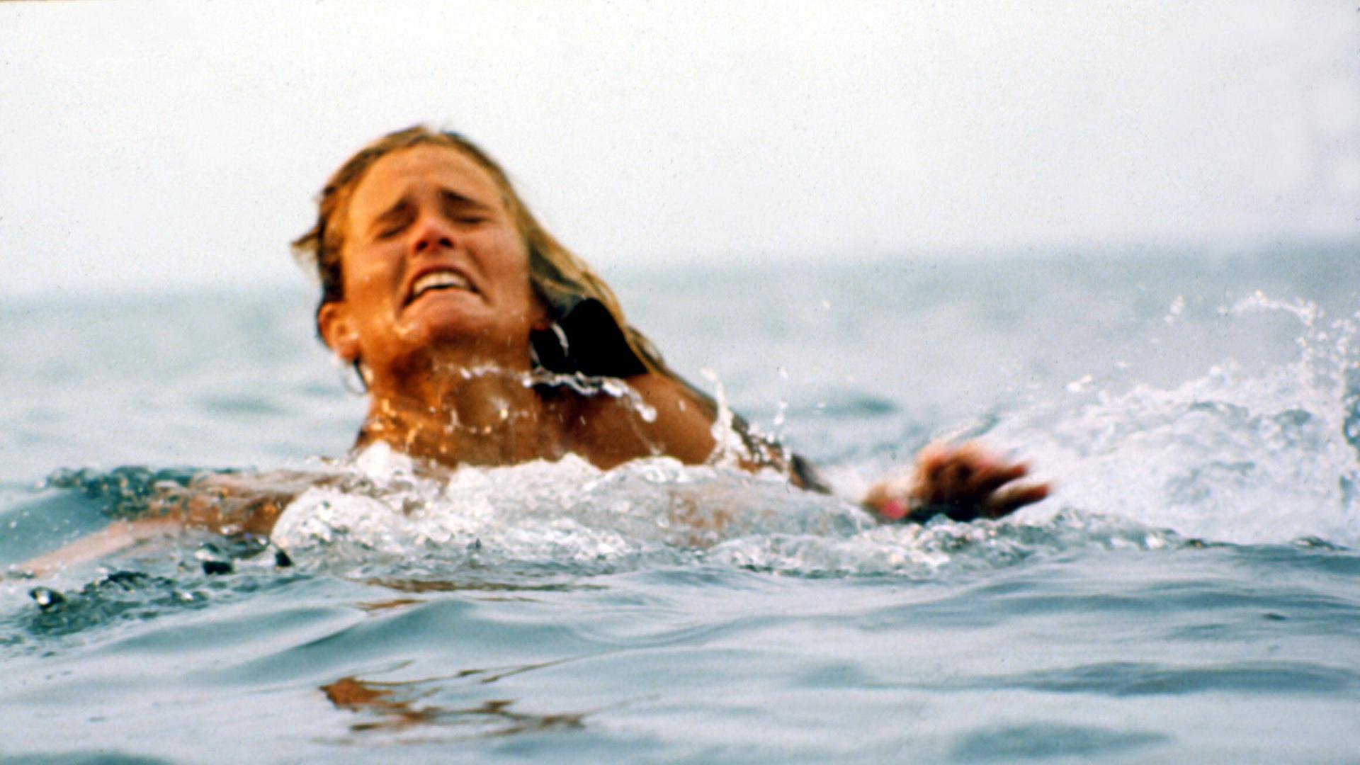 Eine Frau schwimmt im Meer. Sie macht ein verzweifeltes Gesicht.