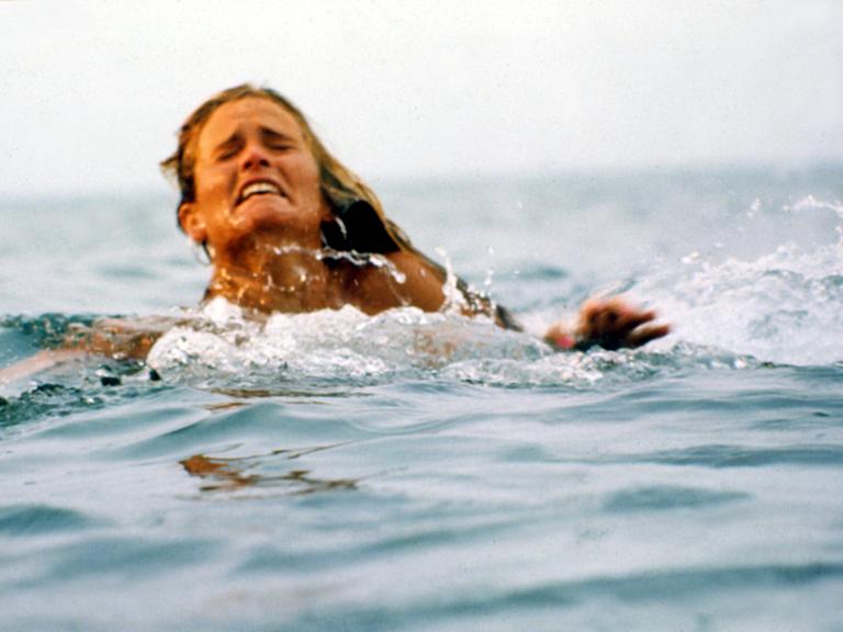 Eine Frau schwimmt im Meer. Sie macht ein verzweifeltes Gesicht.