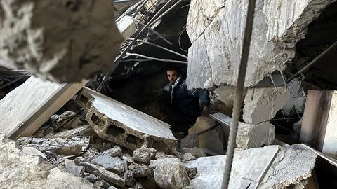 Ein Mann sucht zwischen Trümmern eines zerstörten Hauses nach Menschen