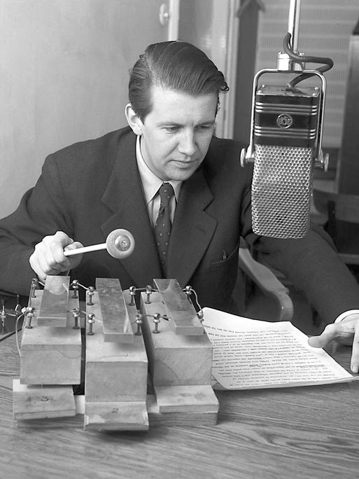 Der schwedische Radiojournalist Folke Olhagen sitzt 1953 hinter dem Mikfrofon eines Radiostudios und spielt dabei mit einem Schlagstock auf drei großen Glockenspiel-Tönen