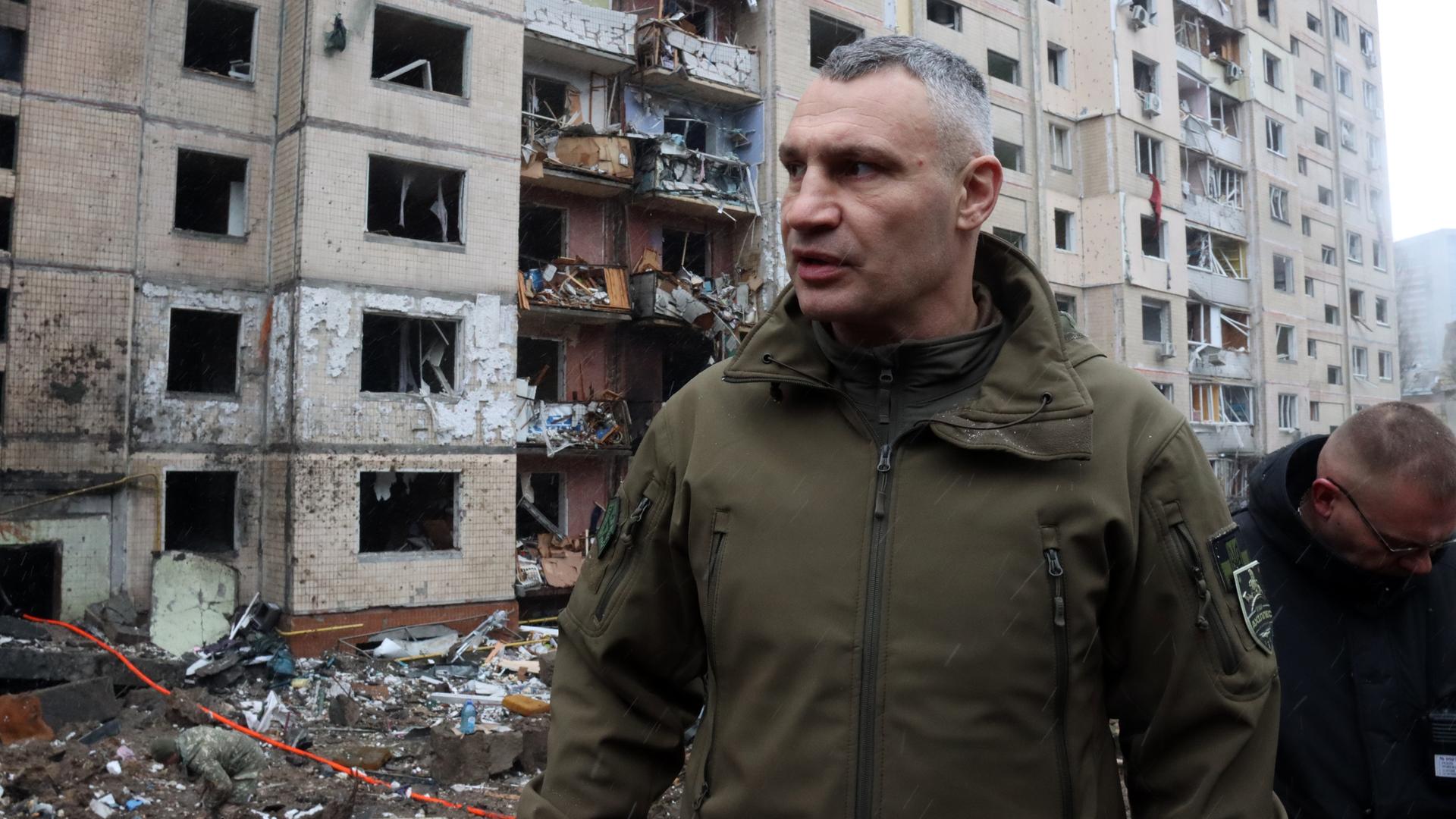Vitali Klitschko, Bürgermeister von Kiew, steht vor einem zerbombten Haus und blickt zur Seite