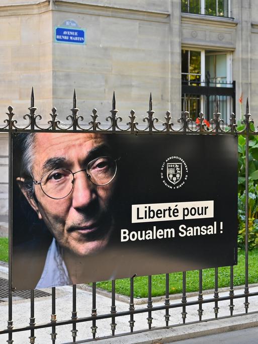 Ein Poster mit einem Porträt von Boualem Sansal und den Worten "Liberté pour Boualem Sansal!" hängt an einem Zaun im 5. Arrondissement in Paris. 