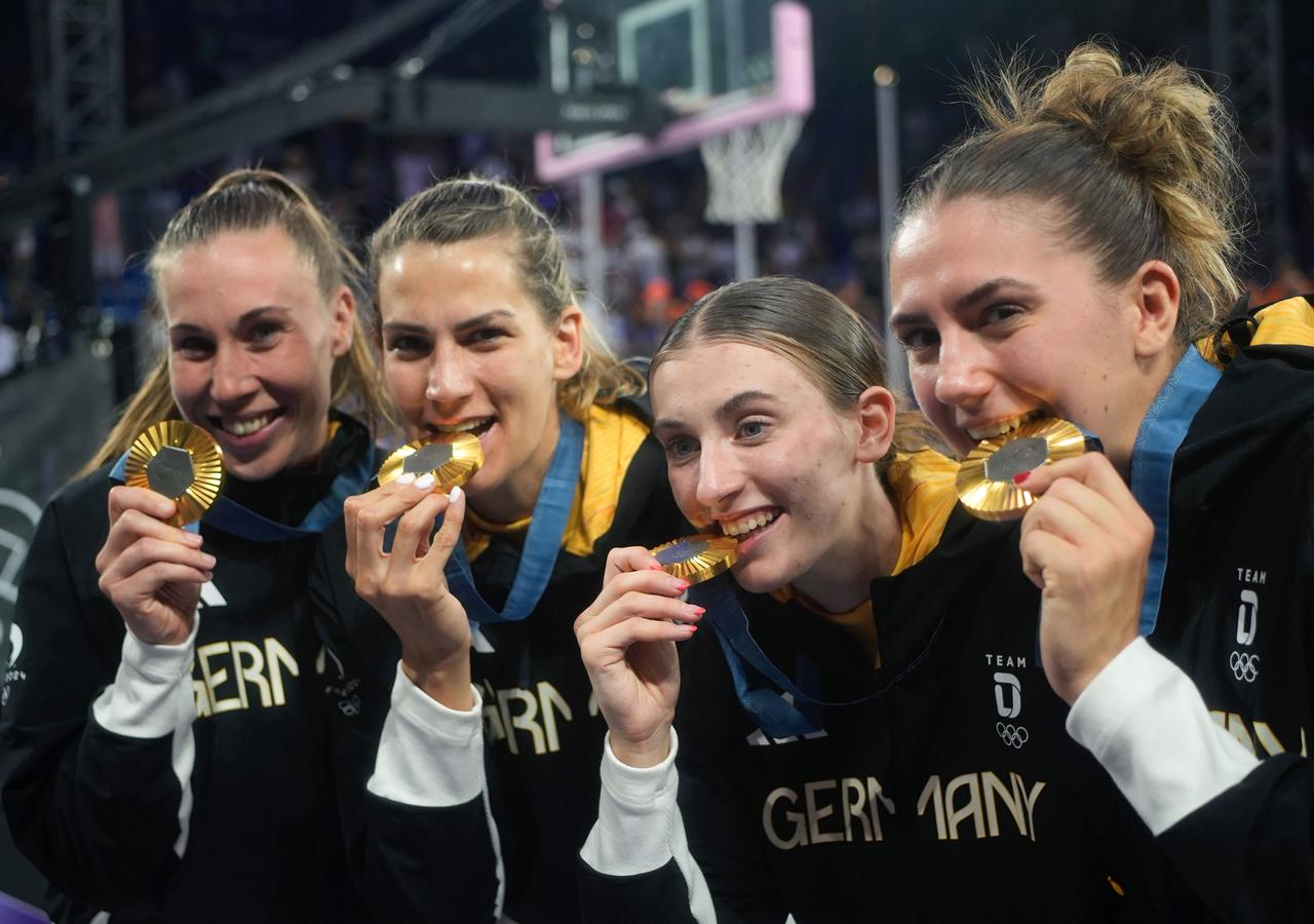 Olympia, Paris 2024, 3x3 Basketball, Damen, Finale, Deutschland - Spanien, Finalrunde, Place de la Concorde, Svenja Brunckhorst (l-r), Sonja Greinacher, Elisa Mevius und Marie Reichert beiÃen nach der Siegerehrung auf ihre Goldmedaille.