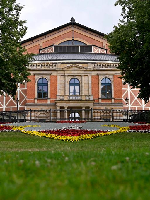 Das Festspielhaus Bayreuth vom Fuße des Grünen Hügels aus fotografiert, davor ein Blumenbeet.