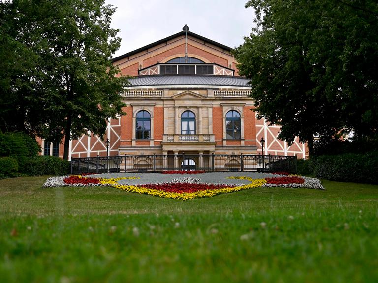 Das Festspielhaus Bayreuth vom Fuße des Grünen Hügels aus fotografiert, davor ein Blumenbeet.