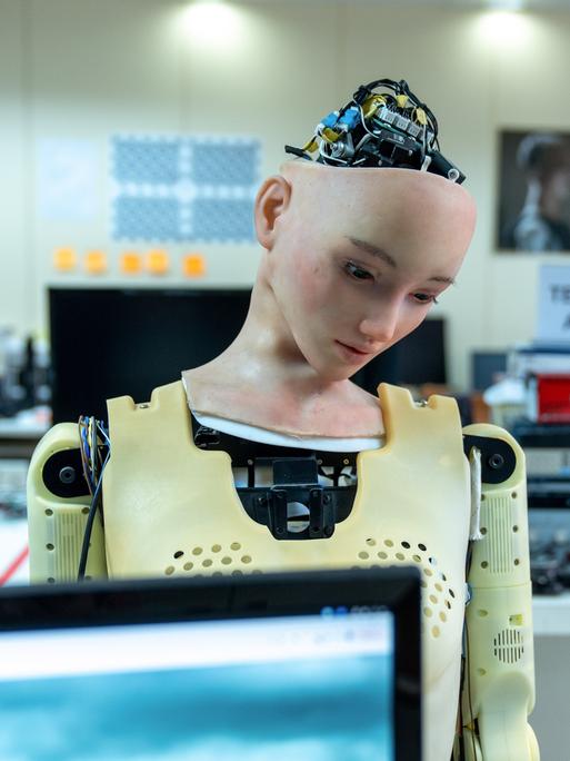 Ein Roboter mit dem Gesicht einer Frau. Aus dem Kopf schauen elektronische Bauteile heraus.