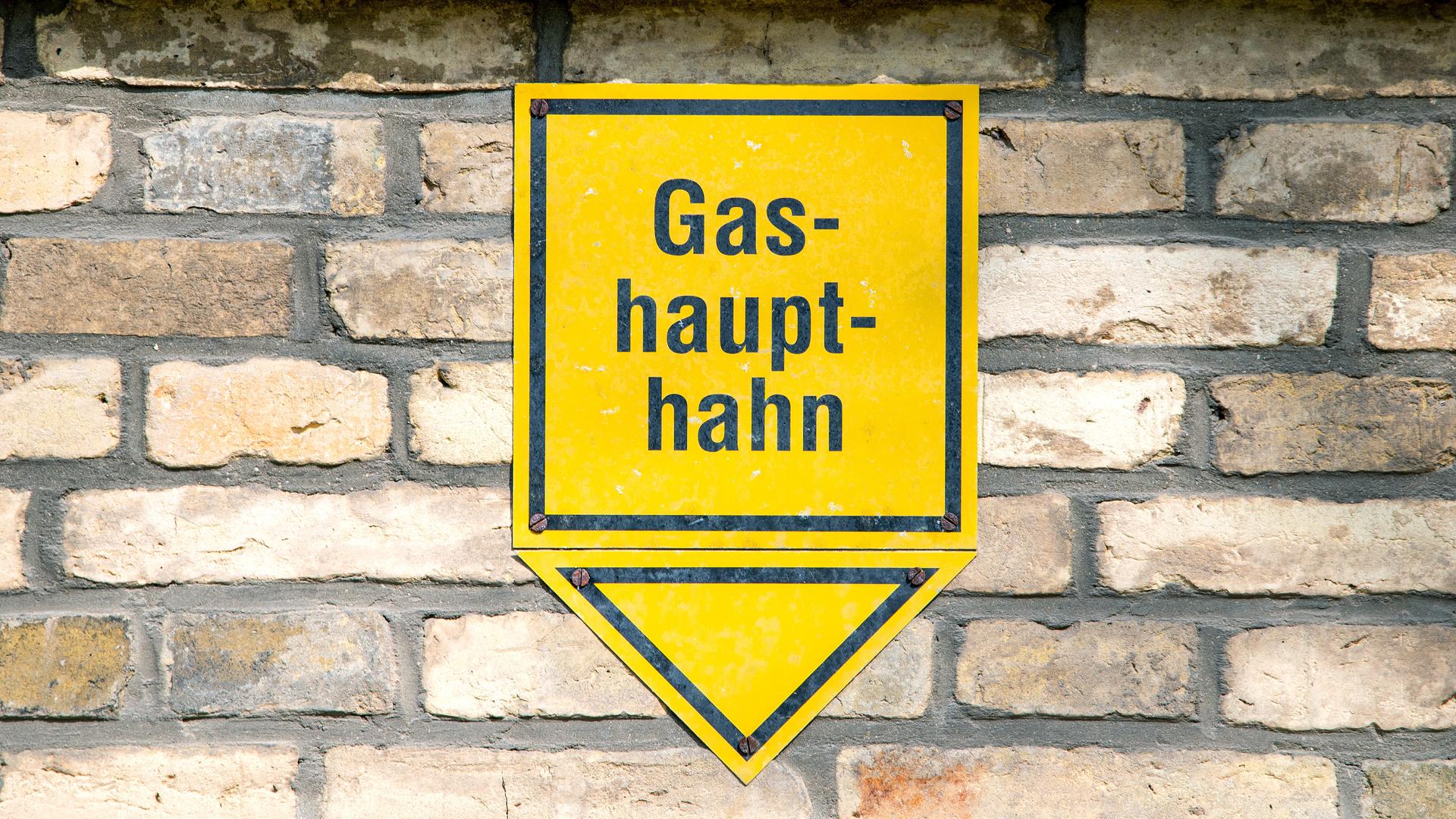 Ein gelbes Hinweisschild mit der Aufschrift "Gashaupthahn" ist an einer Hauswand befestigt. 