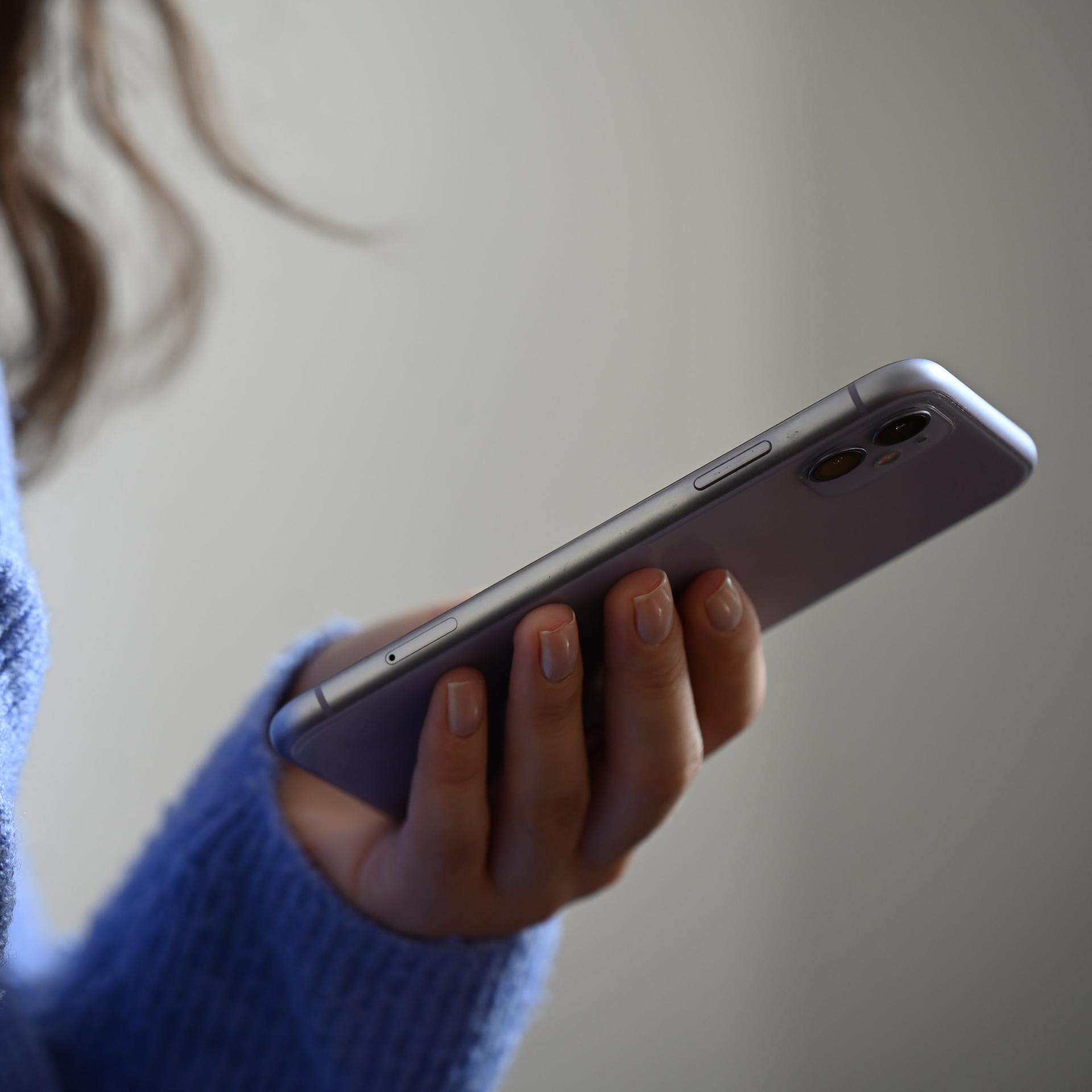 Eine Frau hält ein Smartphone in der Hand. Sie trägt einen blauen kuscheligen Wollpullover.