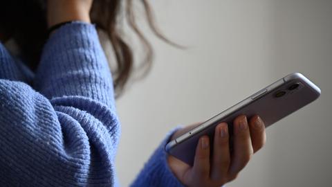 Eine Frau hält ein Smartphone in der Hand. Sie trägt einen blauen kuscheligen Wollpullover.