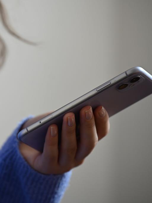 Eine Frau hält ein Smartphone in der Hand. Sie trägt einen blauen kuscheligen Wollpullover.