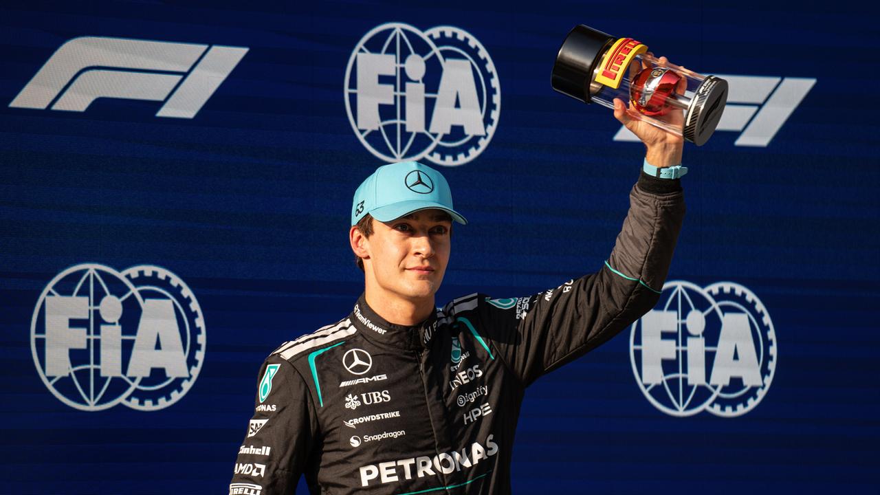 George Russel streckt den Pokal in die Höhe. Dahinteer eine dunkelblaue Wand mit Embelemen des Weltverbands FIA.