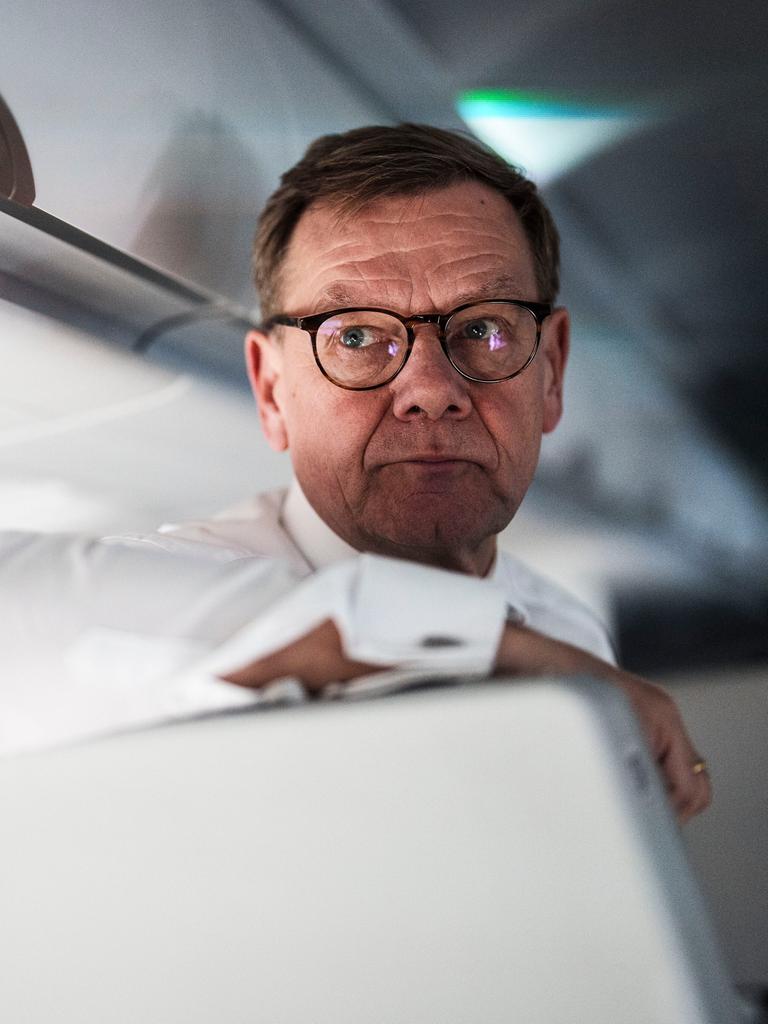 Johann Wadephul steht an einen Sitz gelehnt im Flugzeug und schaut am Betrachter vorbei. Er trägt ein weißes Hemd und eine dunkel umrandete Brille.