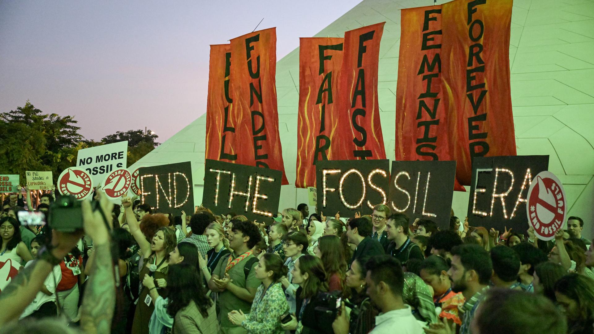 Menschen halten Schilder mit der Aufschrift "End The Fossil Era" während eines Protests. Beim Endspurt der Weltklimakonferenz gibt es nun Bewegung..