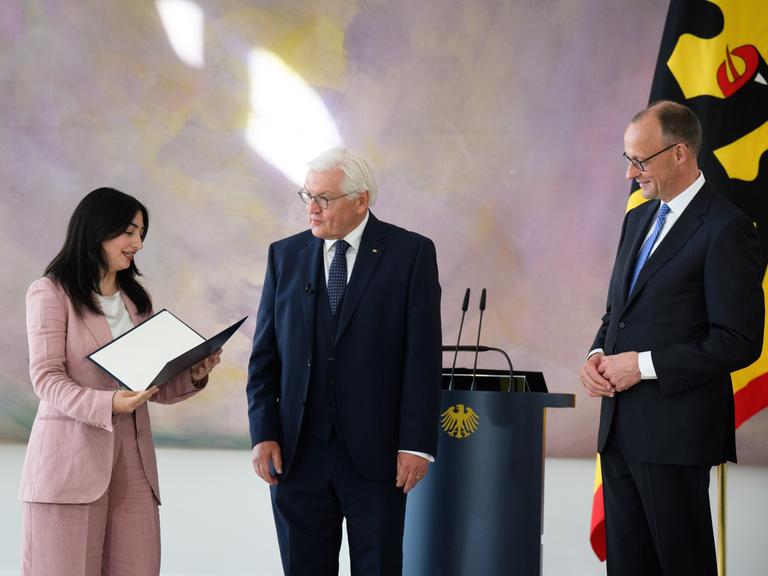 Bundespräsident Frank-Walter Steinmeier (M) übergibt Reem Alabali-Radovan (SPD), Bundesministerin für Wirtschaftliche Zusammenarbeit und Entwicklung, in Anwesenheit von Bundeskanzler Friedrich Merz (r, CDU), im Schloss Bellevue die Ernennungsurkunde.